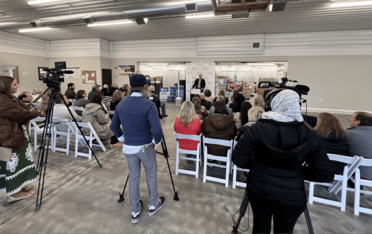 News camera people stand in the back of the room and record a speaker at the Thrive Together announcement.